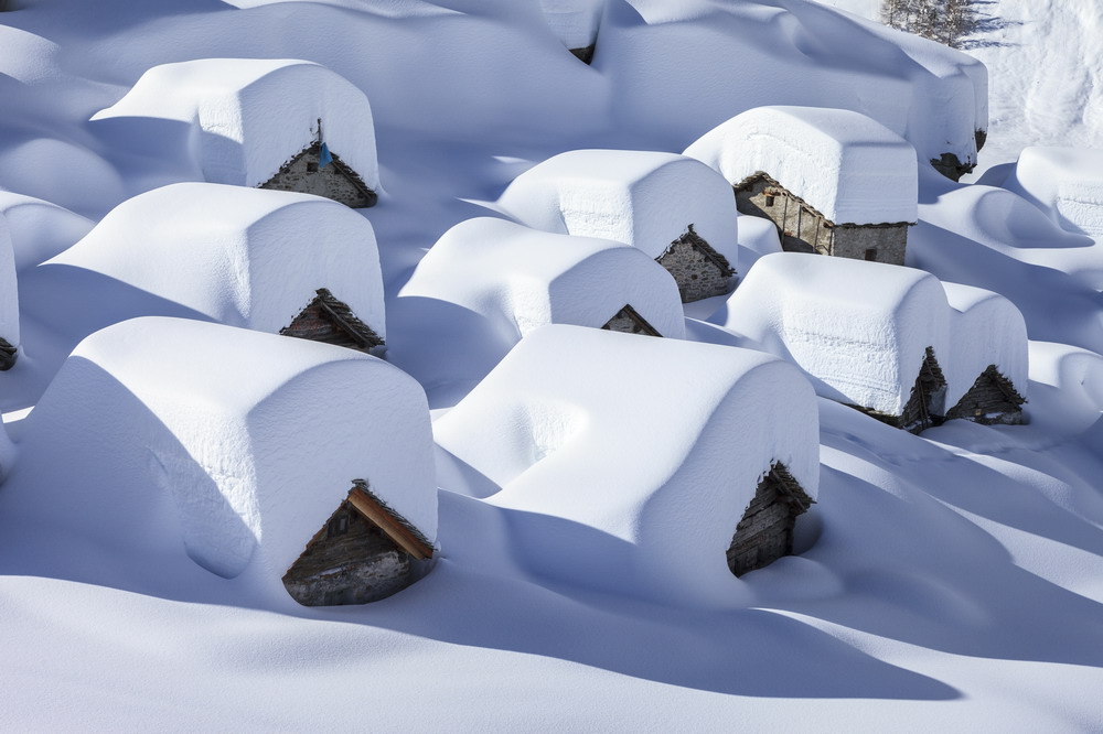 Immagine raffigurante delle baite di montagna coperte da uno strato spesso di neve bianca. Valle del Drogo, località di San Bernardo ai Monti, frazione del Comune di San Giacomo Filippo. Valchiavenna, provincia di Sondrio. Territorio dell'Ecomuseo Val Spluga, uno degli Ecomusei della Lombardia.